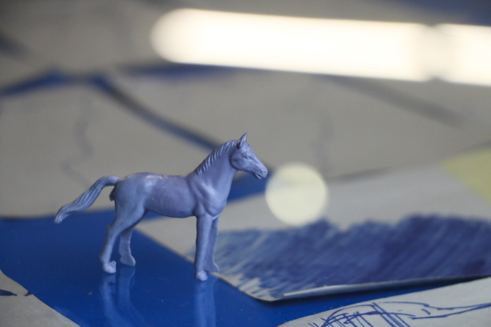 On a blue table which contains drawings is a tiny lilac plastic horse figurine.