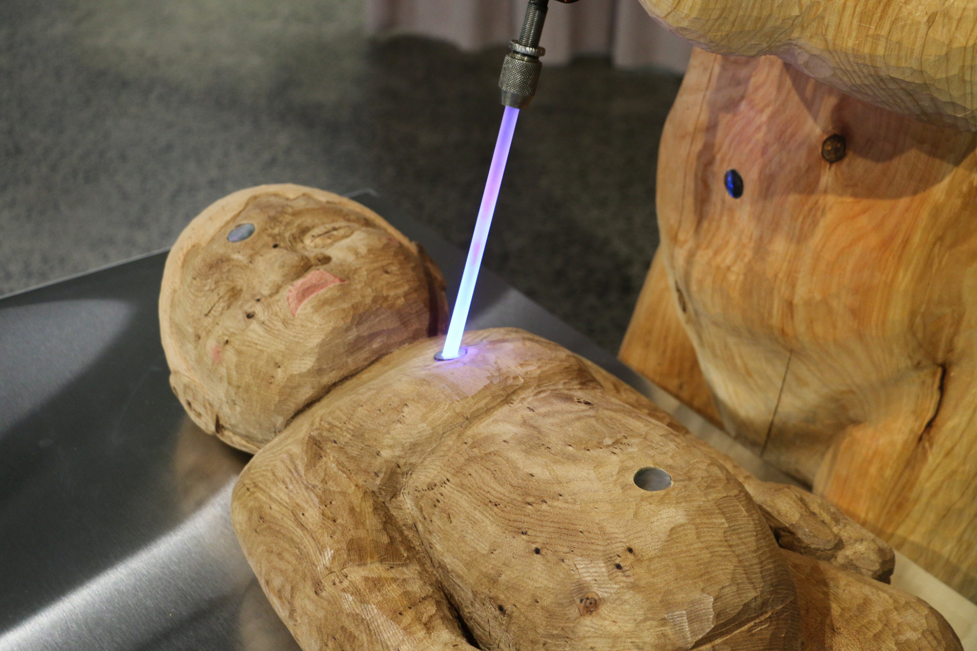 A tekoteko or carved female figure is holding a tool with a beam of light which touches a carved baby figure.