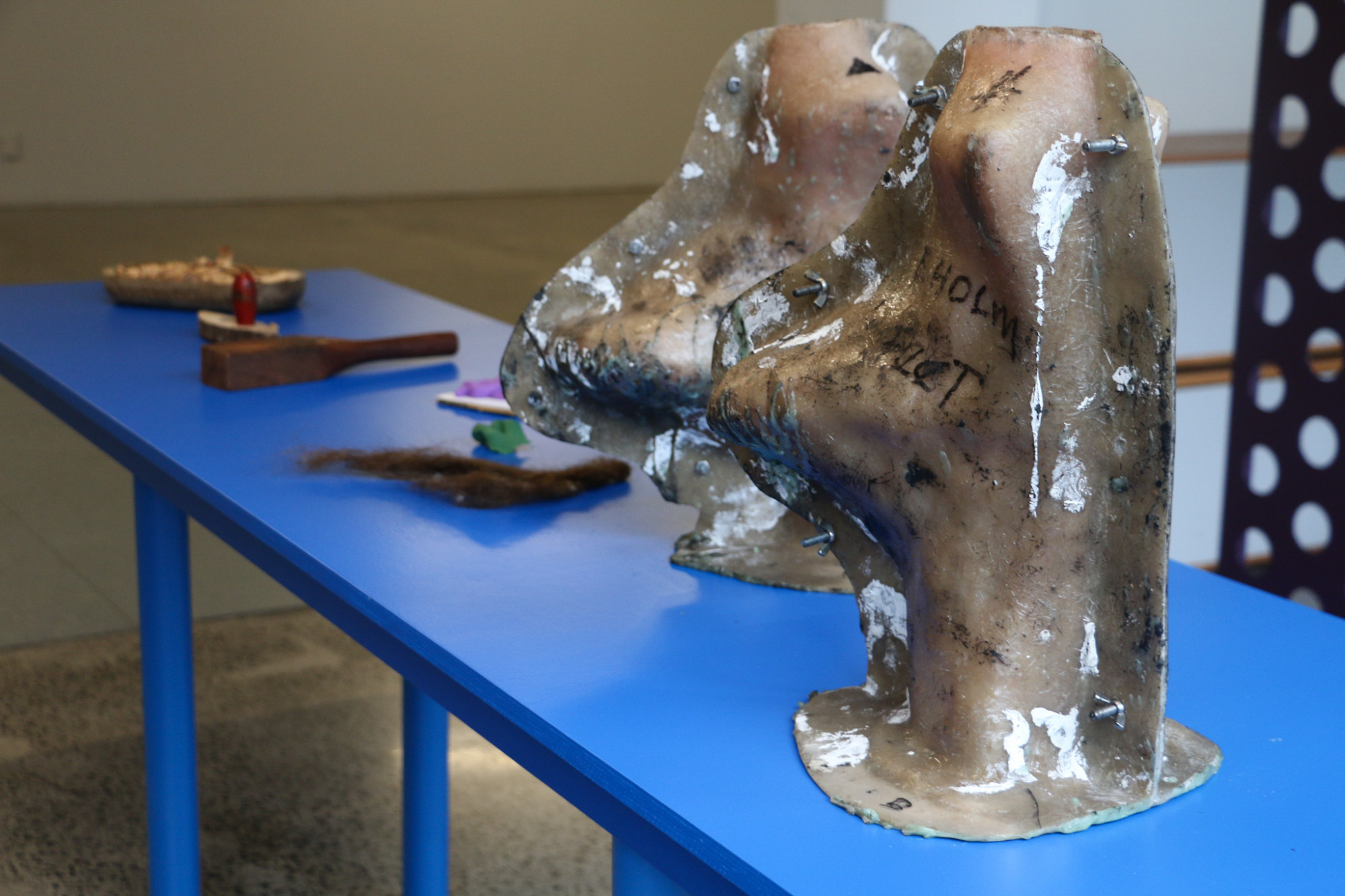 A long blue table holds various items including plastic casts used to make the feet in Erika Holm's artwork Apology.
