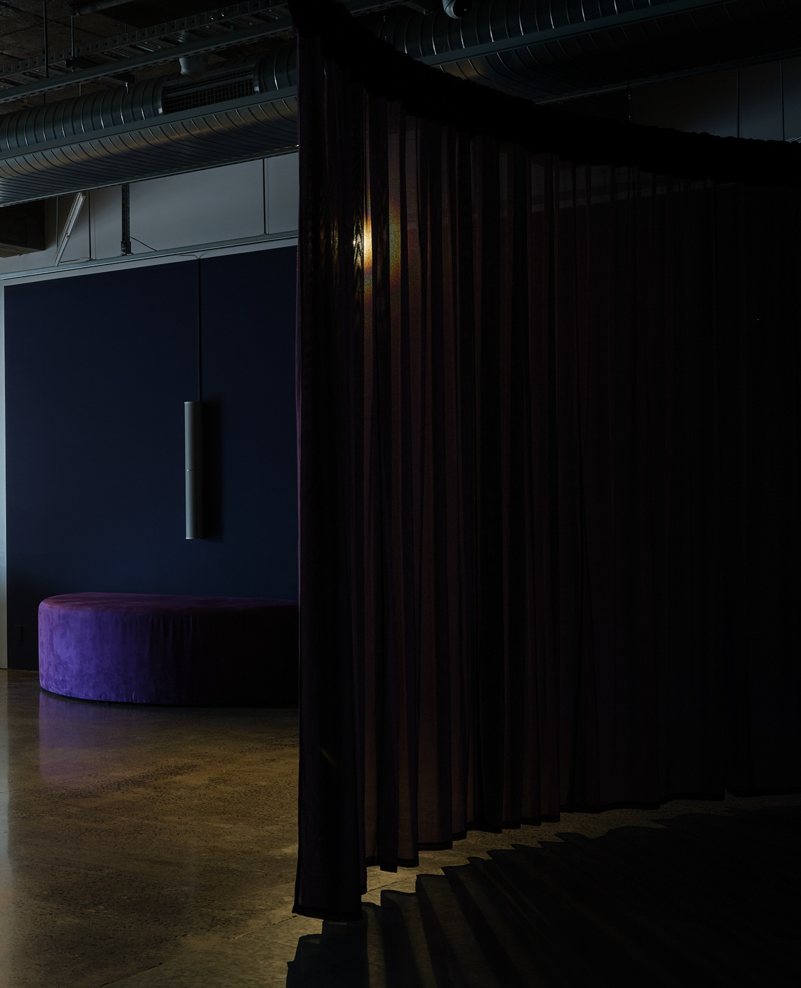 A semi- circle seat against a wall is partially covered by a curtain on curved rails hanging from the ceiling.