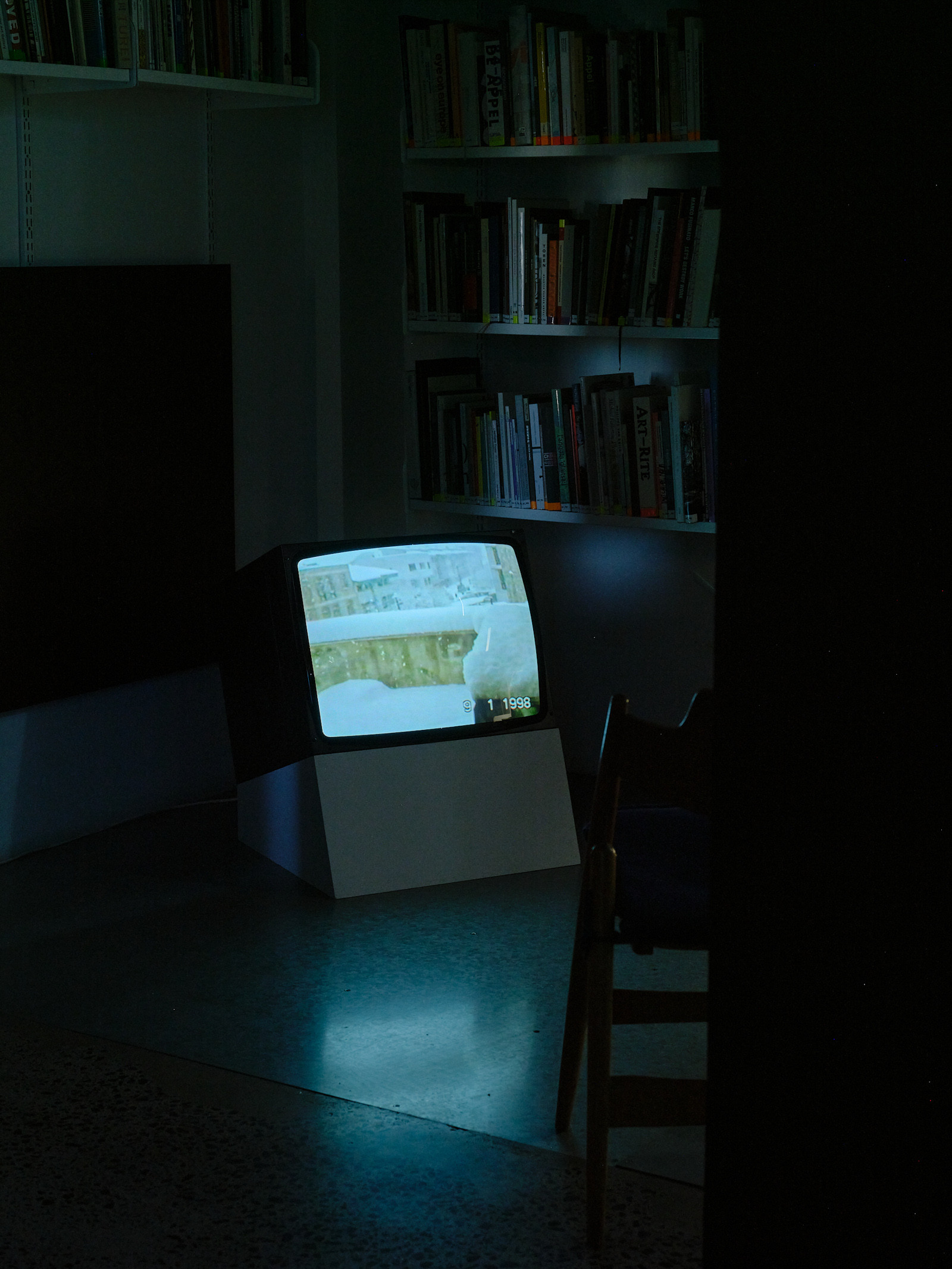 A small television sits on a box with a book shelf behind.
