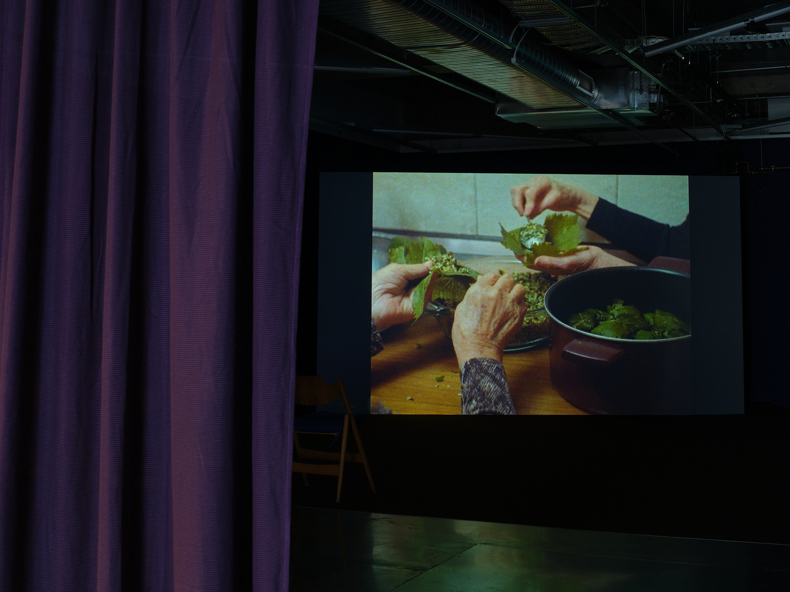 A purple curtain covers part of a screen showing hands making a dish of stuffed leaves