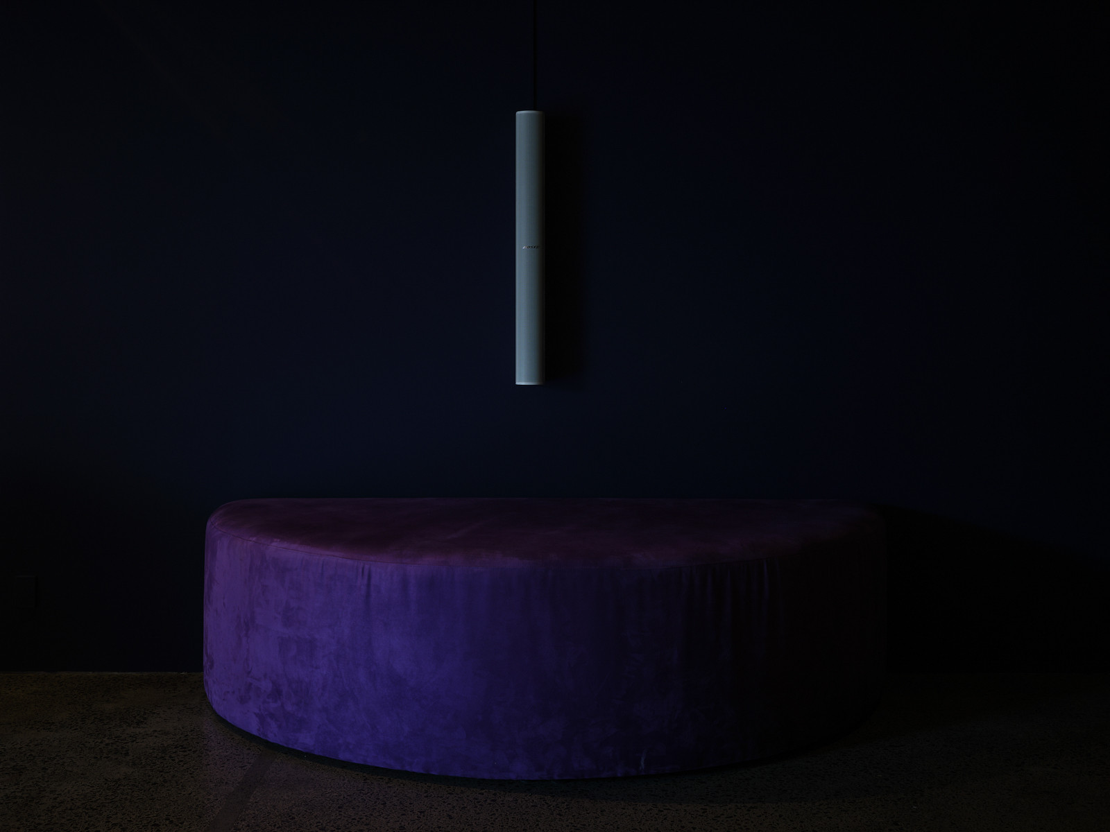 A semi-circle seat placed against a wall with a long speaker hung on the wall above the seat.