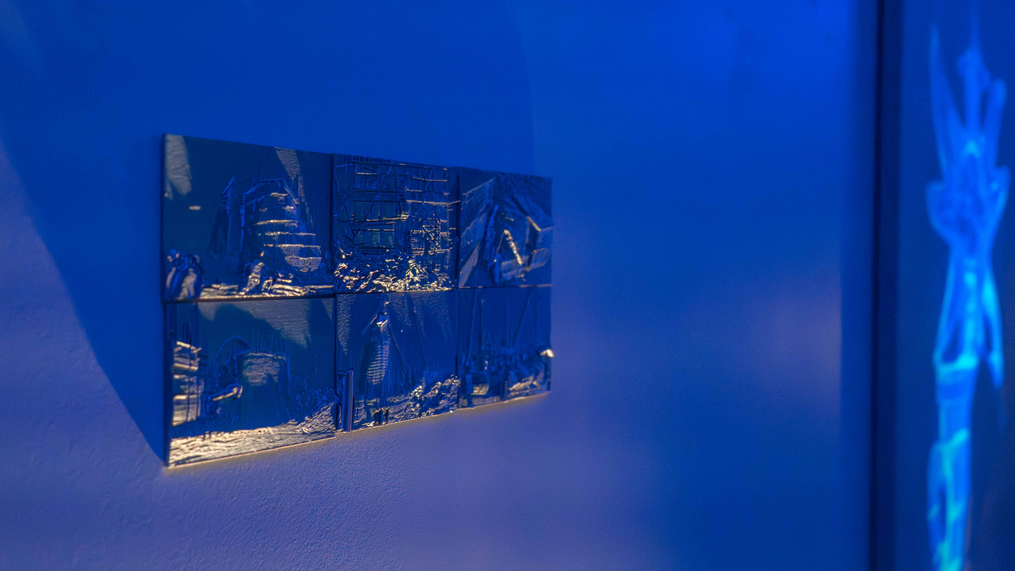 A gentle yellow light shining on six hand-size grey plastic tiles, showing textures of scaffolding buildings in printed in relief carving technique