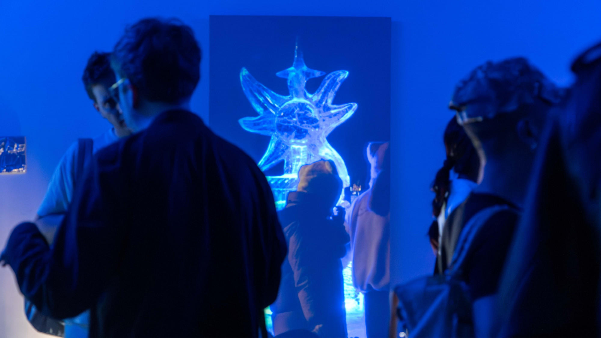 People standing around a long and tall projection, that captured people walking pass a 2 meters tall ice sculpture