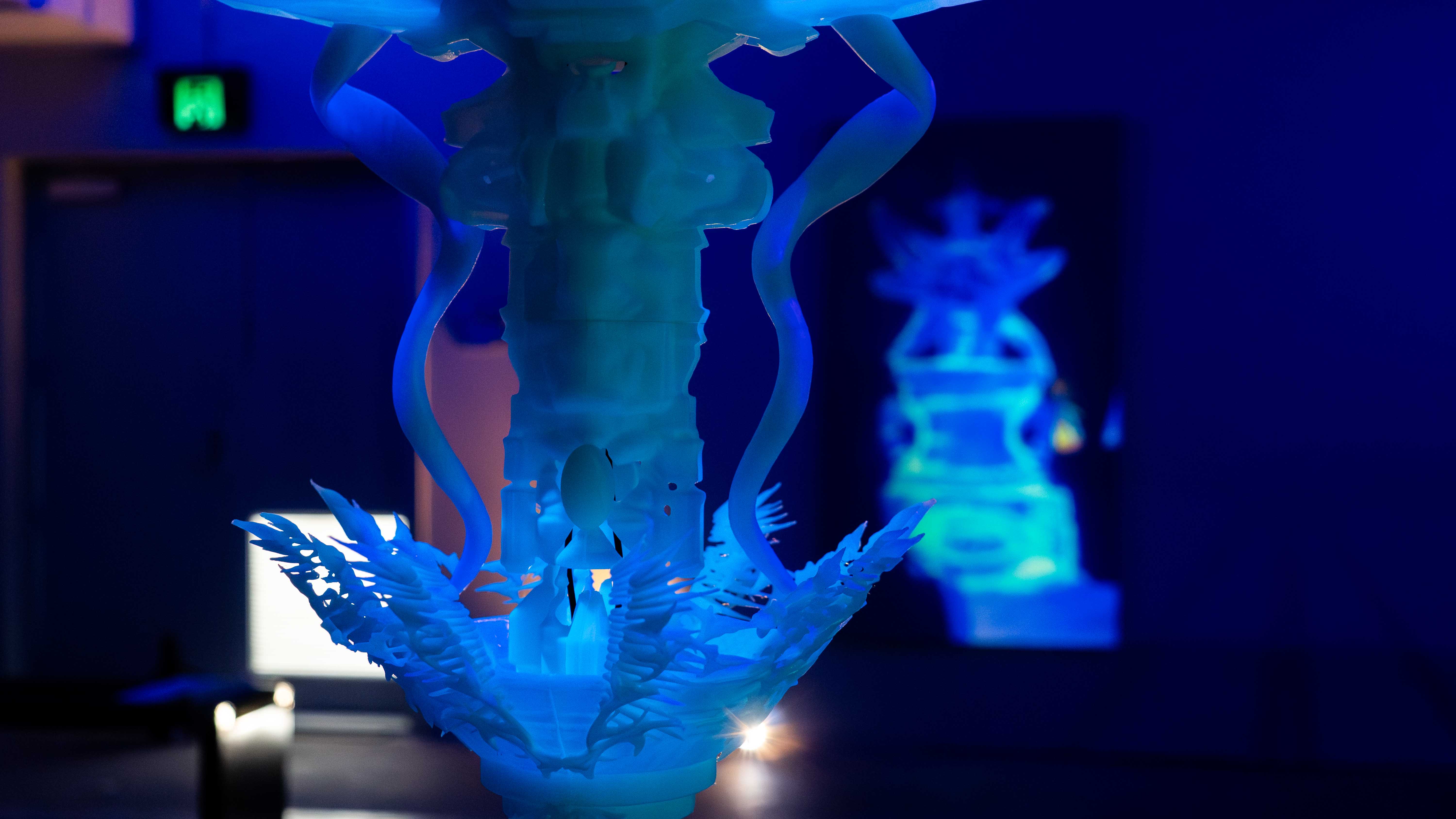 An illuminated sculpture in front of a projection showing a 2 meters tall sculpture made out of ice