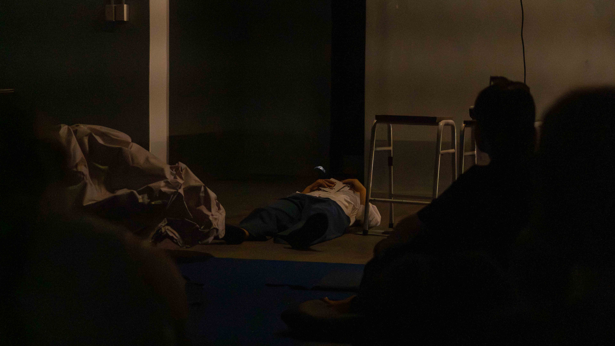 In a dark room, a women in white shirt lying down on the concrete floor