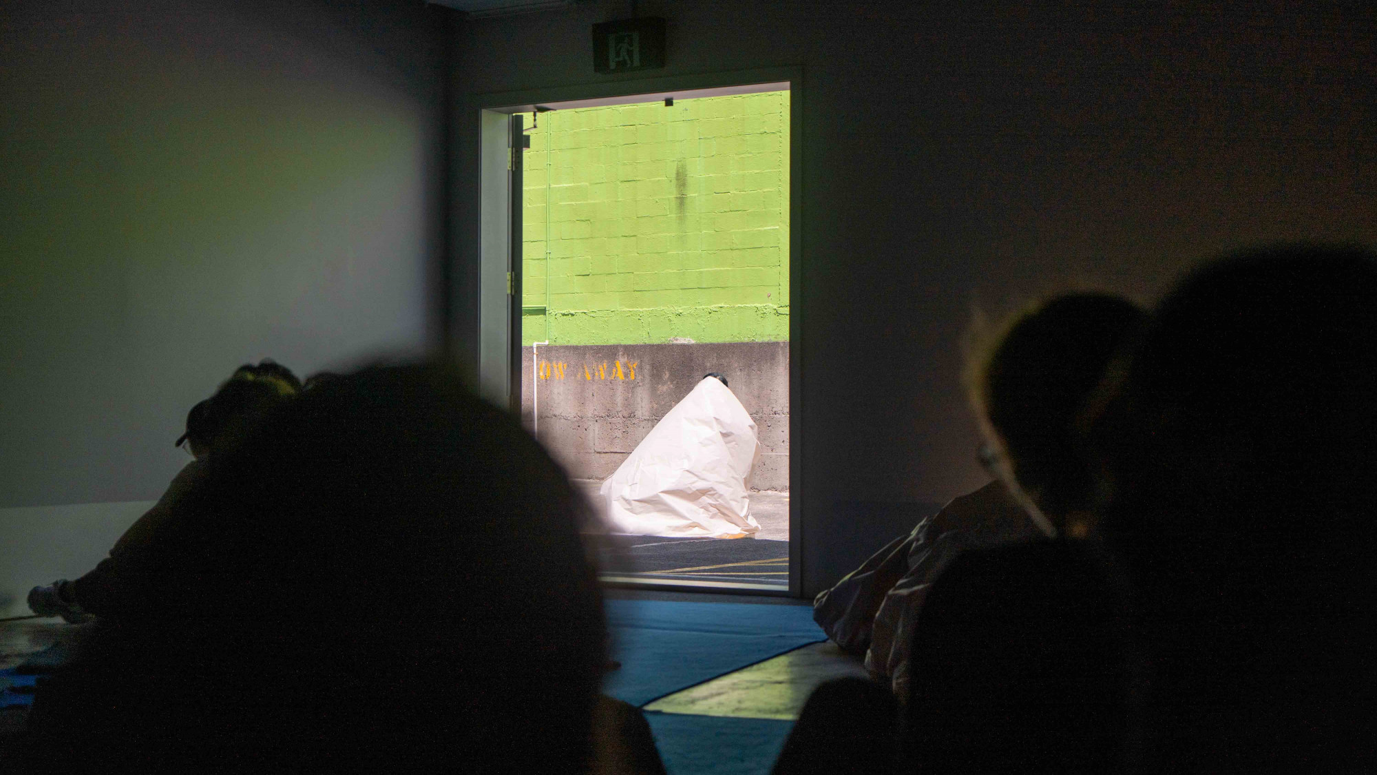 Inside of a carpark with bright green mural, a woman hiding in a big roll of cone-shaped paper only revealing the top of her head