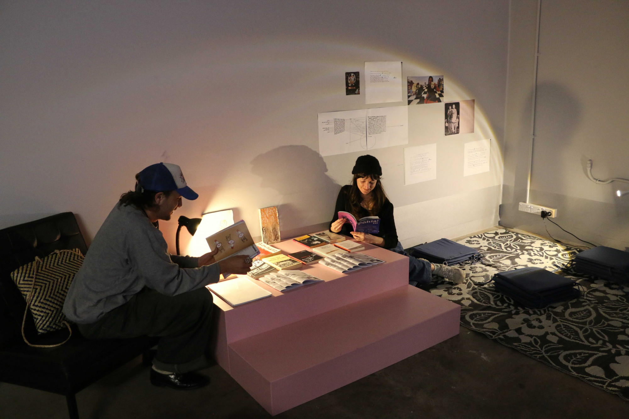 Two people sitting on a couch and on the ground, flipping through publications
