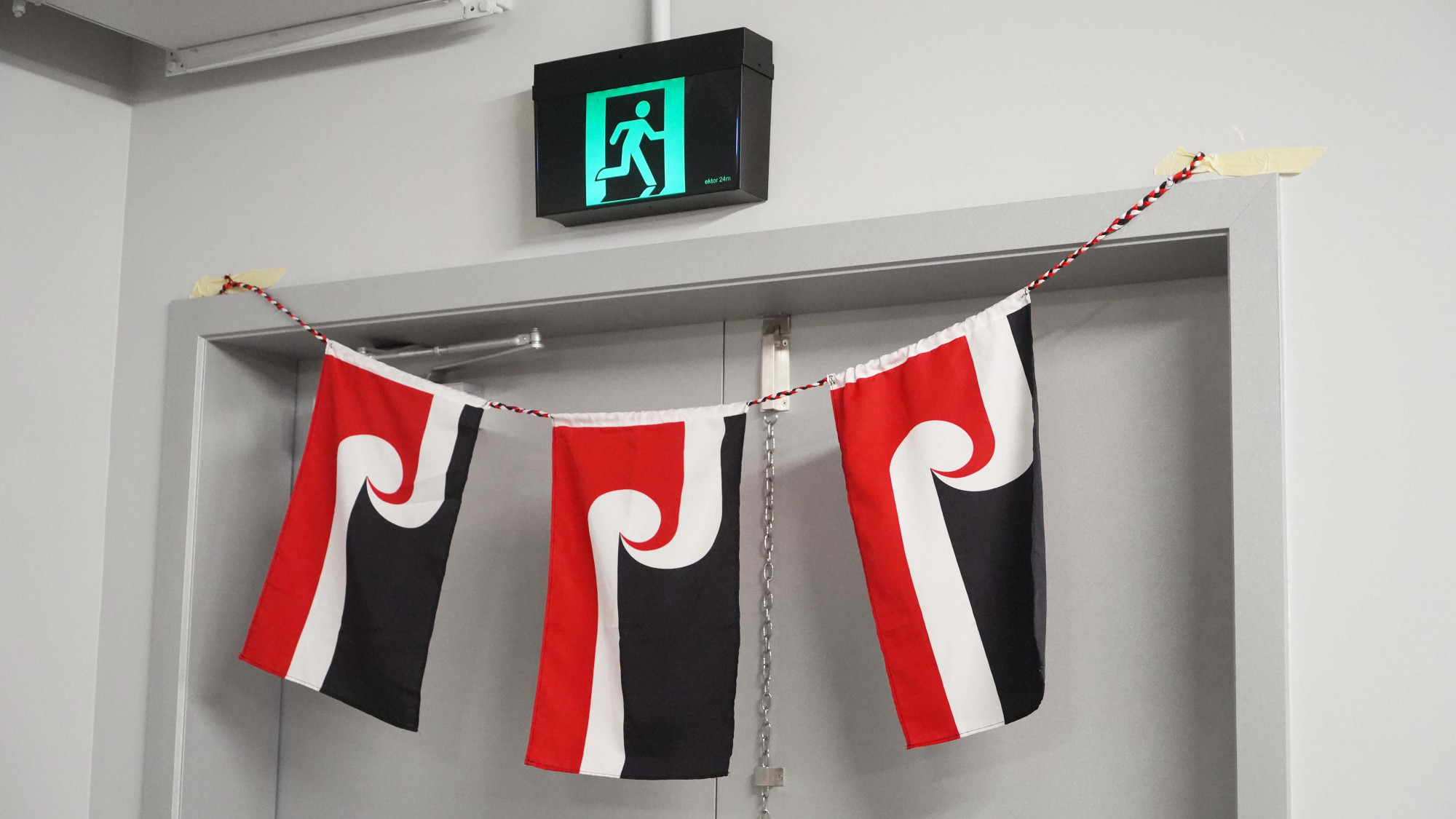 Three Tino Rangatiratanga flags hanging at the entrance of a doorway.