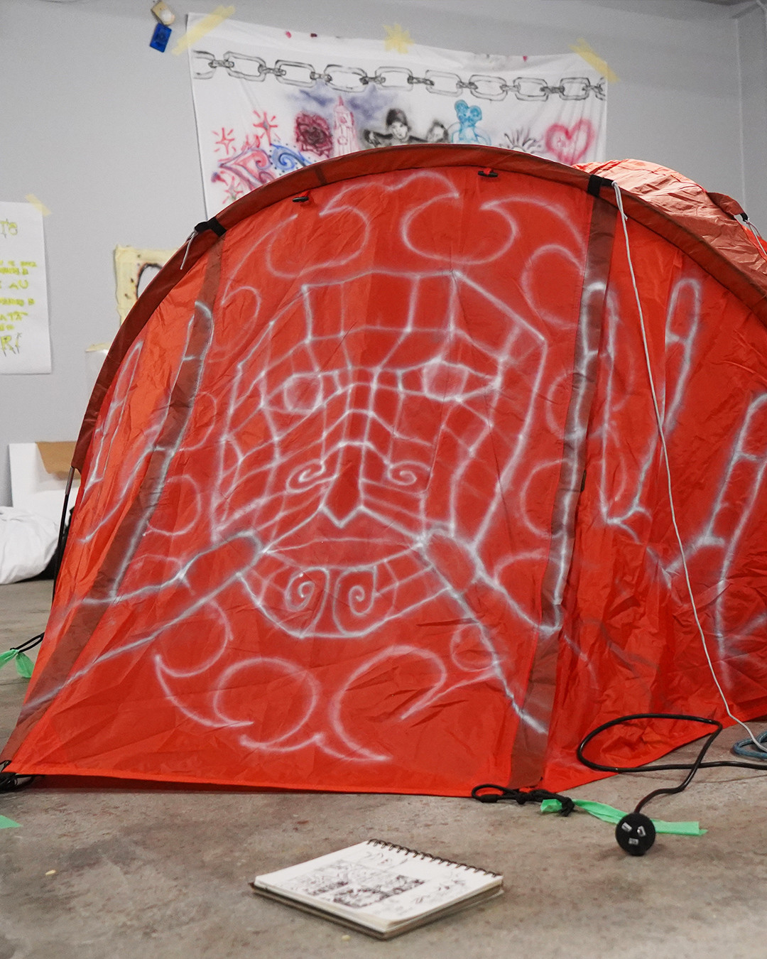 A white airbrush illustration of a spirit with open hands on the front of a big orange tent.