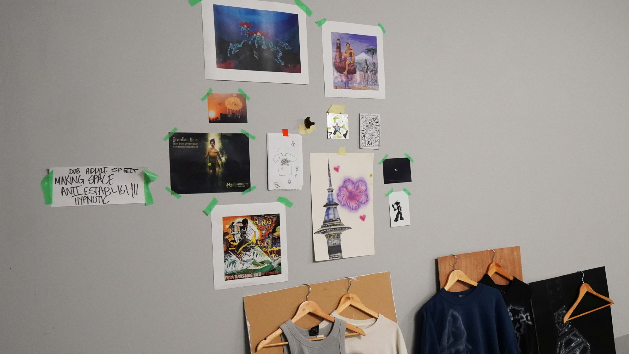 A wall with posters, doodles, images, and spray painted clothes taped to it.